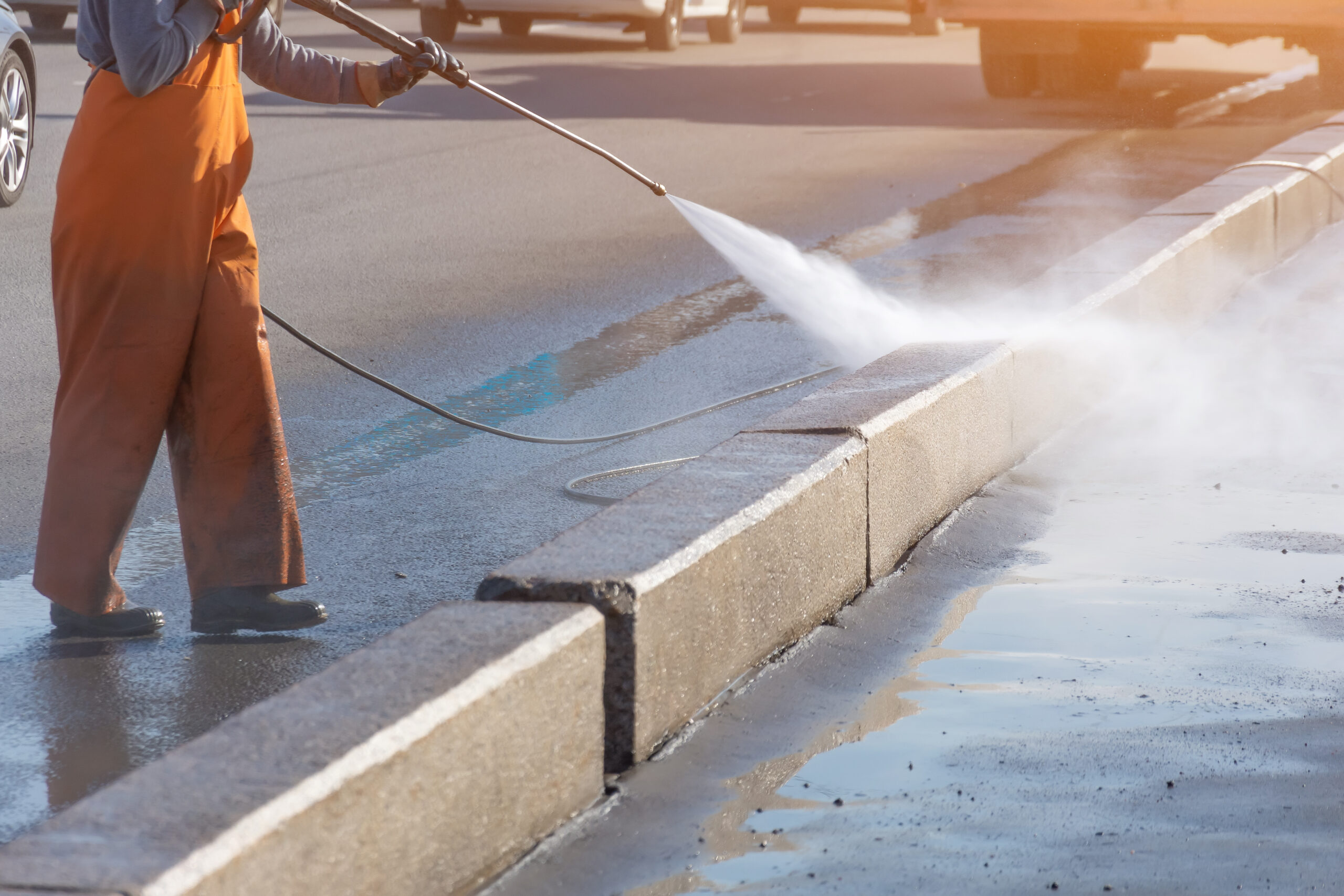 Worker cleaning driveway with gasoline high pressure washer splashing the dirt, asphalt road border. High pressure cleaning